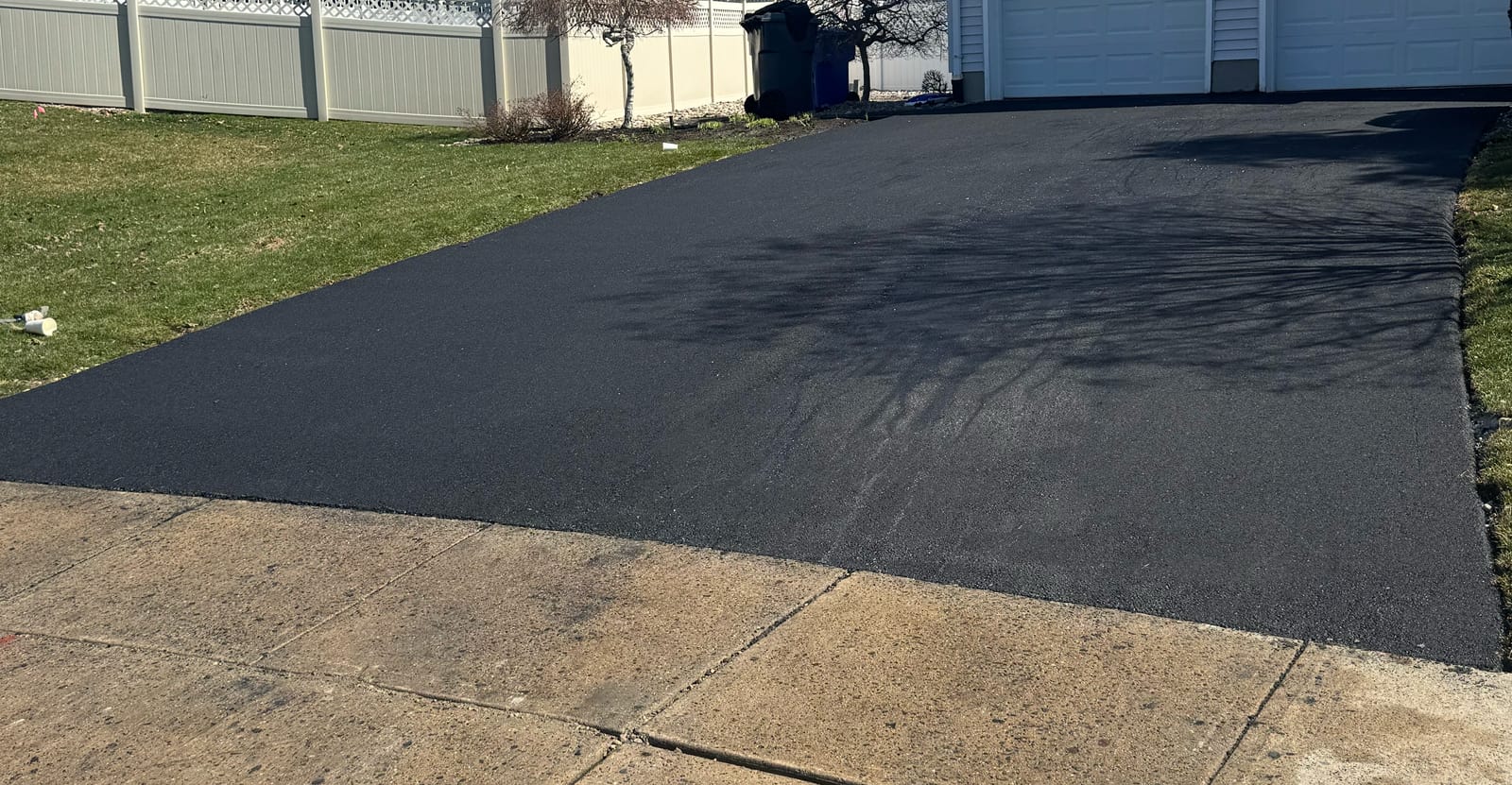 Leveled detail crop of an asphalt driveway, with existing tree shadows and the concrete sidewalk edge.